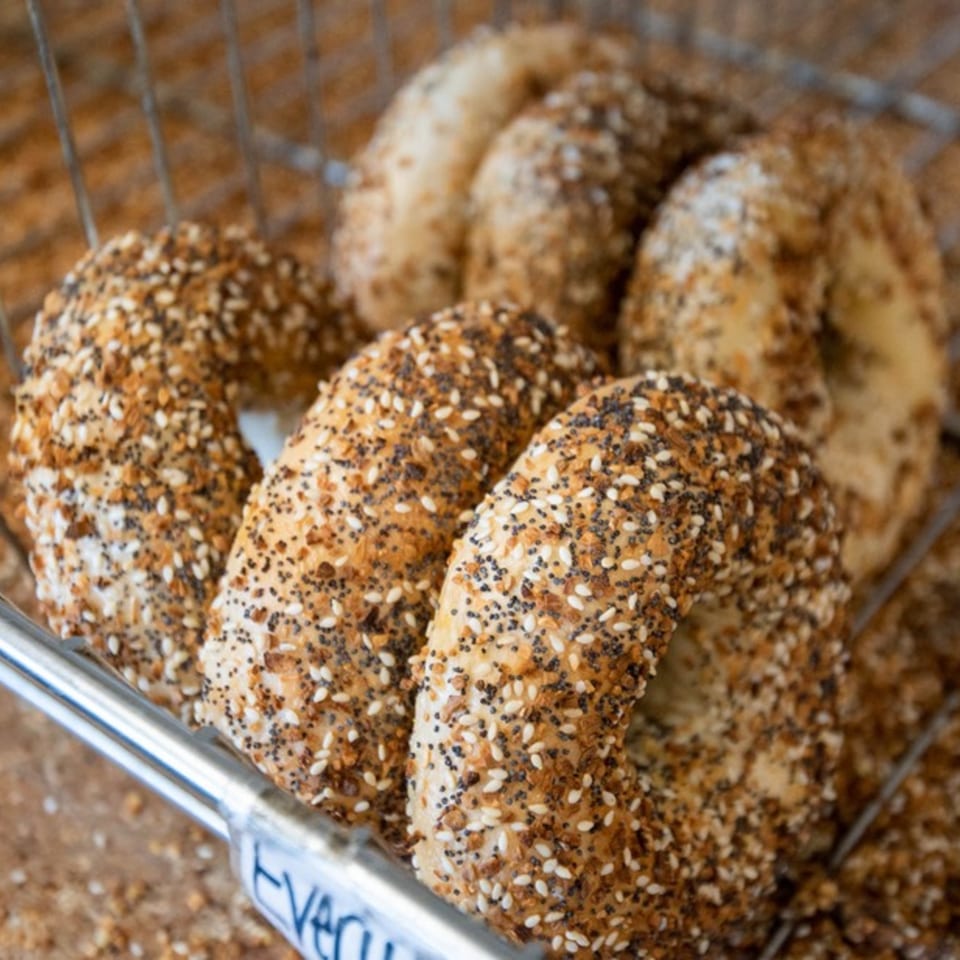 Close-up of several freshly baked everything bagels with seeds in a metal basket at Latham Bagel Shop.