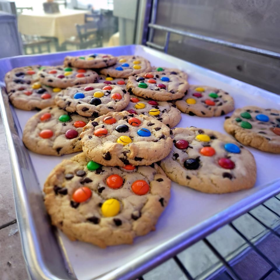 A metal tray filled with freshly baked chocolate chip cookies topped with colorful M&M's.