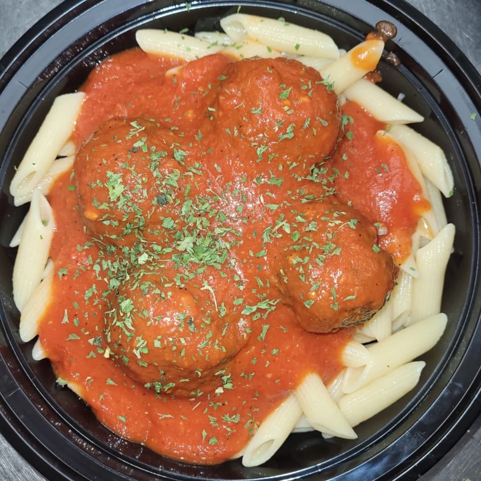 Penne pasta with meatballs and marinara sauce, topped with parsley, in a black bowl.