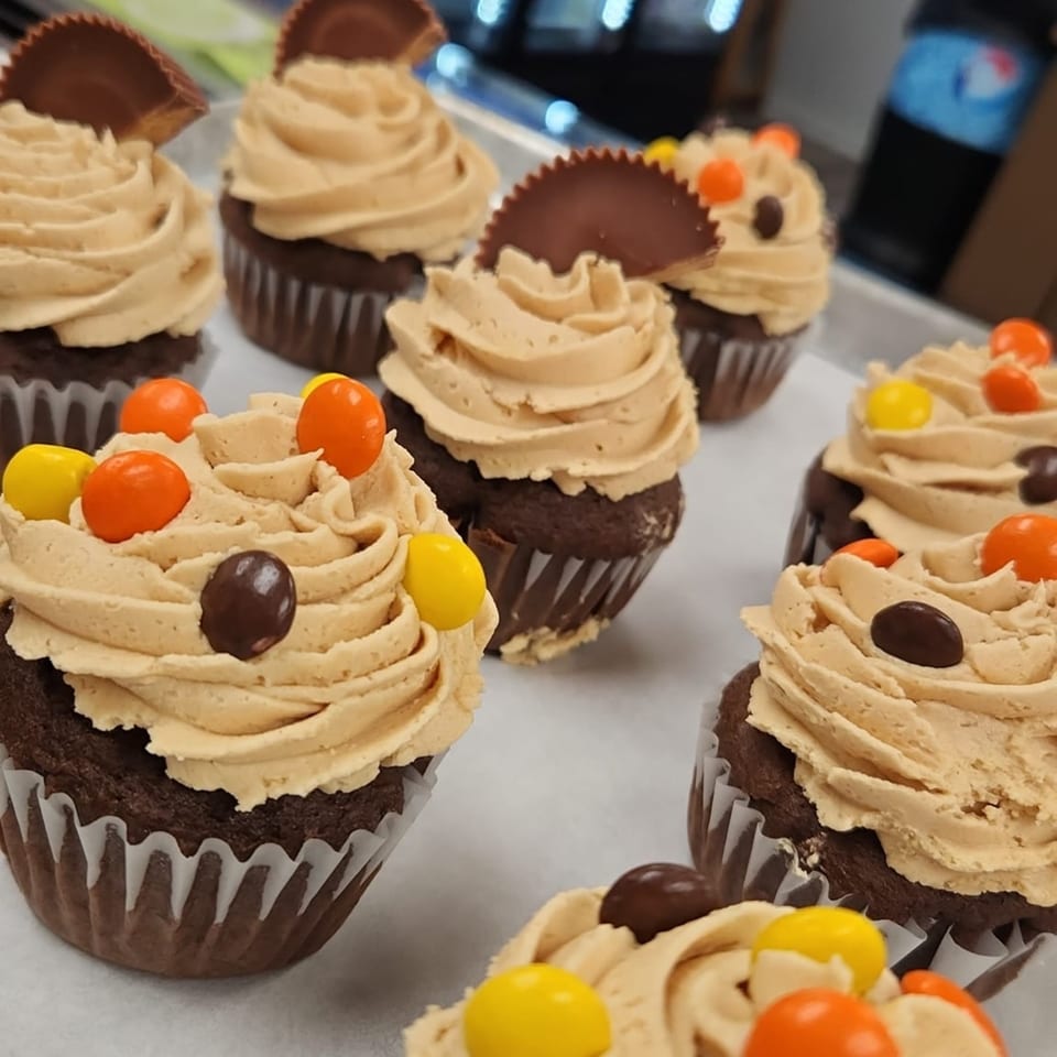 Chocolate cupcakes with peanut butter frosting, some topped with Reese's cups, others with Reese's Pieces.